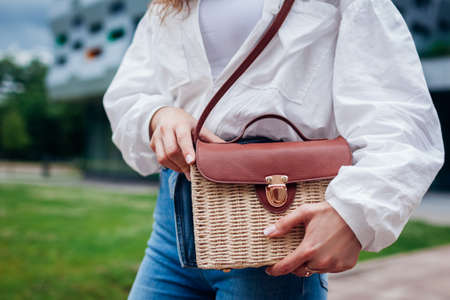 Close-up of stylish female straw handbag. Young woman wearing outfit and accessories outdoors. Summer fashionable purseの写真素材