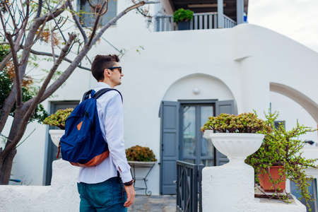Man traveler walking in village looking at architecture on Santorini island, Greece. Tourist backpacker renting traditional greek houseの写真素材