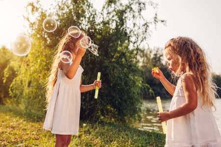 Little girls sisters blowing soap bubbles in spring park. Kids having fun playing games outdoors. Children summer activitiesの写真素材