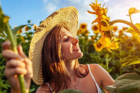 Young happy woman walking in blooming sunflower field wearing hat feeling free smelling flowers and admiring landscape. Summer vacationの写真素材