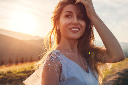 Beautiful bride wearing blue wedding dress in mountains at sunset. Happy young woman enjoys summer landscape. Close up portraitの写真素材