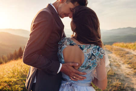 Young loving wedding couple hugging in mountains at sunset. Portrait of happy bride and groom in summer Carpathians. Back view of open back dressの写真素材