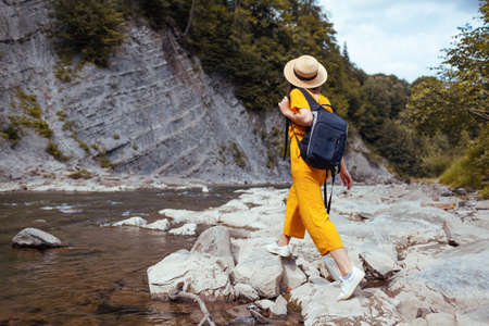 Young tourist woman hiking by mountain river enjoying landscape. Traveler walking with backpack along rocks. Summer vacationの写真素材