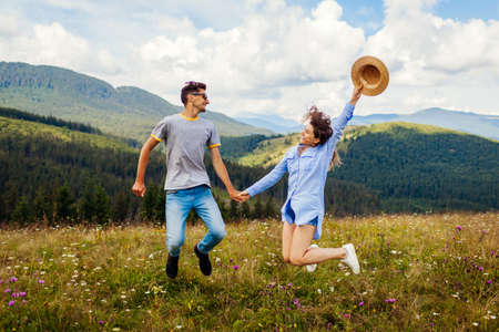 Young loving couple of tourists jumps feeling happy in Carpathian mountains enjoying view. Travelers have fun. Summer vacationの写真素材