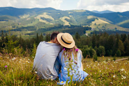 Couple of hikers relaxing sitting in Carpathian mountains enjoying landscape. Travelers kiss. Summer vacation. Back viewの写真素材