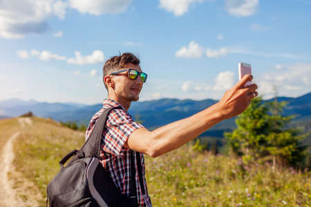 Man hiker taking selfie photo with smartphone in Carpathian mountains on hill peak. Traveler...