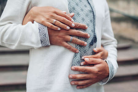 Wedding newlyweds couple hugging wearing rings on fingers. Bride and groom wear traditional embroidered ukrainian shirts. Close up of handsの写真素材