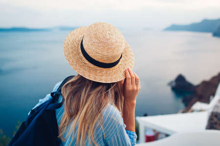 Tourist woman walking on Santorini island, Greece enjoying sea landscape. Traveler with backpack enjoys Caldera view in Oiaの写真素材