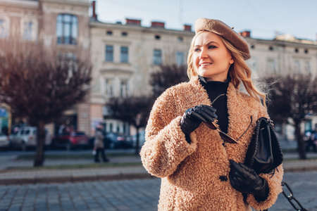 Stylish woman wearing teddy coat beret holding purse on city street. Autumn fashion female accessories and clothes. Portrait of girl in vintage outfitの写真素材