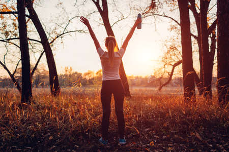 Runner raised arms after workout feeling free and happy succeeded in training. Woman admiring sunset in autumn forest. Healthy lifestyleの写真素材