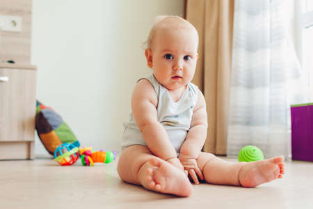 Little newborn baby playing with toys sitting on floor at home. Kid looking at camera. Infant portraitの写真素材