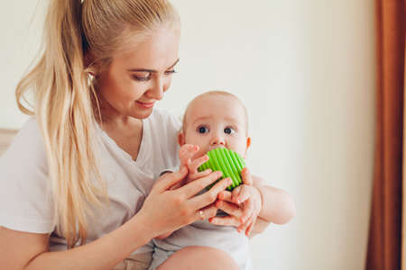 Mother playing with her newborn baby son at home. Family having fun. Infant biting toy ballの写真素材