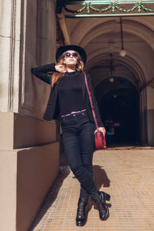 Portrait of stylish woman wearing black jacket, hat, sunglasses holding purse outdoors. Female beauty, autumn fashion.の写真素材