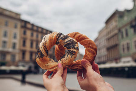 Couple of tourists holding bagels obwarzanek, traditional polish cuisine prezel snack on Market square in Krakow. Traveling Europeの写真素材