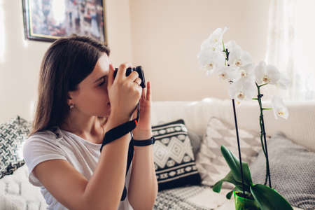 Woman photographer takes picture of blooming orchid using camera. Freelancer works from home during coronavirus covid-19の写真素材