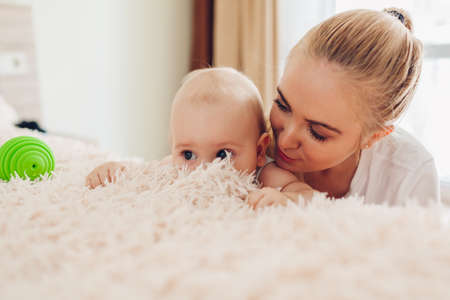 Mother playing with her newborn baby son at home. Family having fun. Infant touching blanket on bed. Spaceの写真素材