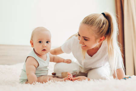 Mother playing with her newborn baby son at home. Family having fun sitting on bed in bedroom. Mothers dayの写真素材