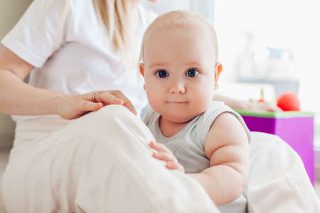 Newborn baby sitting by mothers knees. Family relaxing at home. Kid looking at camera. Mothers dayの写真素材