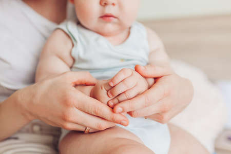 Close up of kids hands. Woman sitting on bed with her newborn baby son hugging child. Family relaxing at home.の写真素材