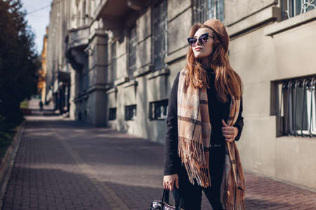 Autumn beauty fashion. Stylish woman wearing beige beret, sunglasses and scarf holding handbag. Fall accessories.の写真素材