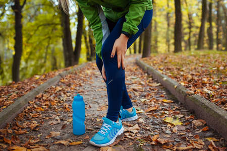 Runner injured leg during intense training in autumn park. Woman feels knee pain. Workout hurtの写真素材
