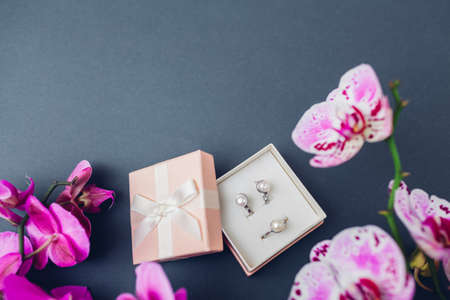 Set of jewellery. Silver ring and earrings with pearls in gift box with purple orchid on white background. Fashionable accessories. Jewelry as presentの写真素材