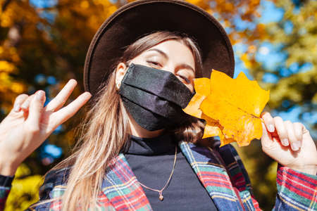 Portrait of woman wearing mask in fall park during coronavirus covid-19 pandemic and taking selfie....