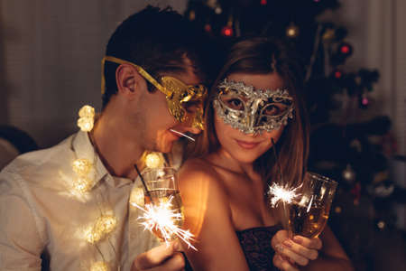 Christmas and New year masquerade party concept. Couple in love burning sparklers by illuminated...