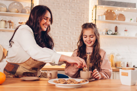 Family drinking tea with cookies at home. Mother and daughter laughing dipping biscuits in cupsの写真素材