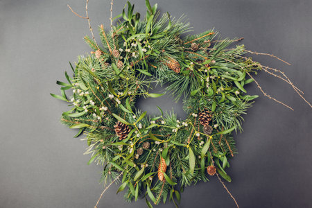 Christmas and New Year wreath made of fir, pine, mistletoe branches, cones decorated with golden ornaments, toys, bows on grey background.の写真素材