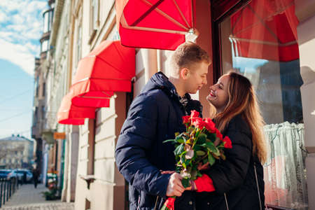 Valentines day couple hug outdoors. Man giving red roses flowers to girlfriend on date in city. Womens dayの写真素材