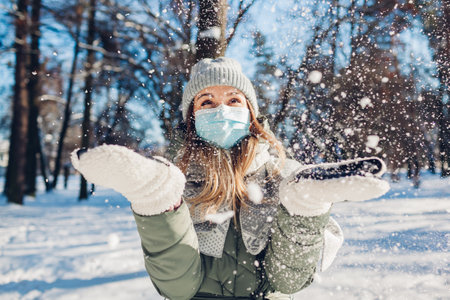 Winter portrait of happy woman in protective mask playing with snow outdoors.の写真素材