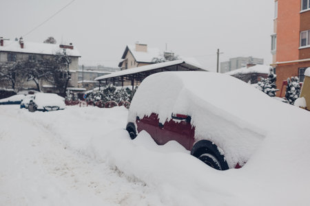 Cars covered with snow during snowfall in city. Automobiles stuck in heaps after winter blizzardの写真素材