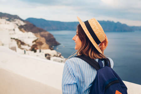 Tourist woman walking on Santorini island, Greece enjoying sea and city landscape. Traveler with backpack admires Caldera view in Oiaの写真素材
