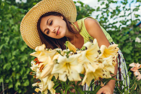 Woman smelling and enjoying flowers in garden. Gardener taking care of yellow lilies. Girl growing...