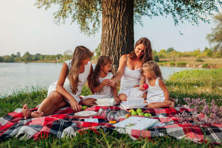 Mother's day. Family having picnic by spring river at sunset. Mother, grandmother and kids laughing...