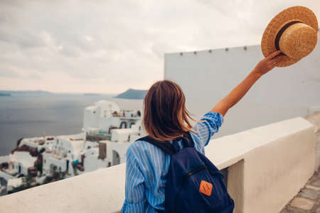 Tourist woman walking on Santorini island, Greece enjoying sea and city architecture landscape. Traveler with backpack admires Caldera view in Oiaの写真素材