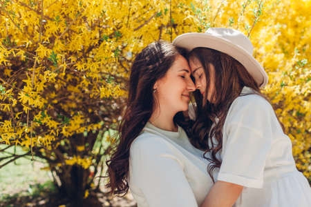 Happy woman holding her daughter in blooming spring garden by yellow flowering bush. Family walking outdoors. Mother and kid smileの写真素材