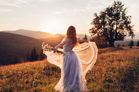 Beautiful bride dancing in blue wedding dress in mountains at sunset. Woman enjoys landscape holding gownの写真素材