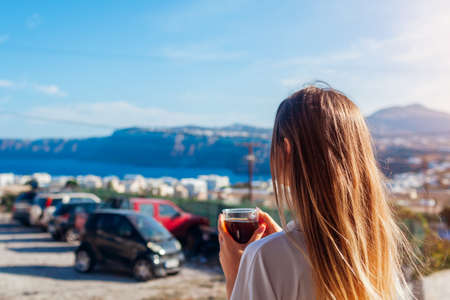 Woman relaxing on terrace drinking morning coffee enjoying Santorini mountain seashore landscape in Akrotiri. Summer vacationの写真素材