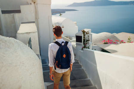 Santorini traveler man walking along narrow street in Fira, Greece enjoying sea view. Tourism, summer vacationの写真素材
