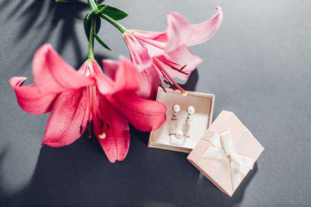 Set of pearl jewellery in pink gift box with flowers. Silver earrings and ring with lily on grey backgroundの写真素材