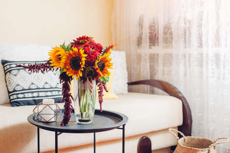 Bright bouquet of sunflowers and zinnia flowers put in vase in living room. Interior and home decor. Fall yellow red orange autumn blooms on tableの写真素材