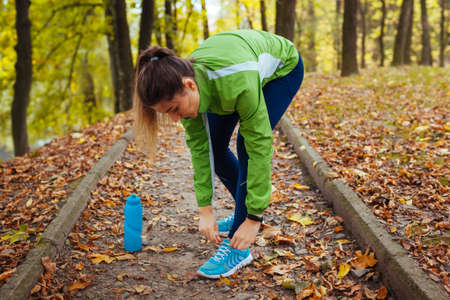 Runner tying shoe laces in autumn park. Woman training with water bottle. Active healthy sportive lifestyle. Workout. Fall activities.の写真素材