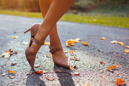 Close up of female shoes. Woman wears stylish brown high-heeled shoes in autumn park standing among falling leaves. Fashionの写真素材