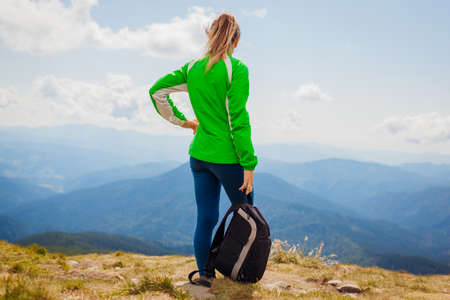 Trip to Carpathian mountains. Happy woman tourist hiker with backpack admires view on top of Hoverla enjoying landscape and fresh air. Traveling in summer Ukraineの写真素材