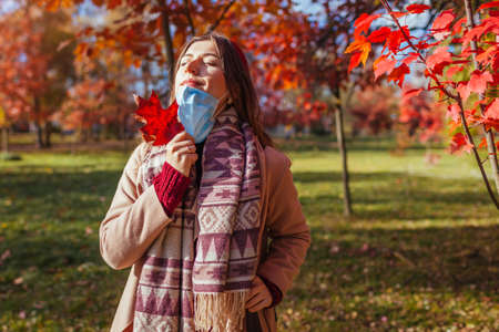 Happy young woman takes protective mask off outdoors during pandemic in empty fall park breathing and enjoying sun.の写真素材