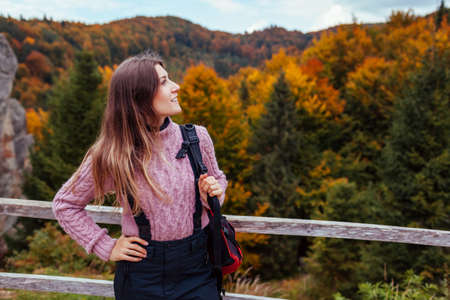 Woman traveler with backpack enjoys rocks and forest in autumn Carpathian mountains. Fall tourism in Ukraine. Hiking and recreationの写真素材