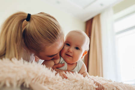 Woman playing on bed with her baby. Mother hugging kid. Family relaxing at home spending time togetherの写真素材