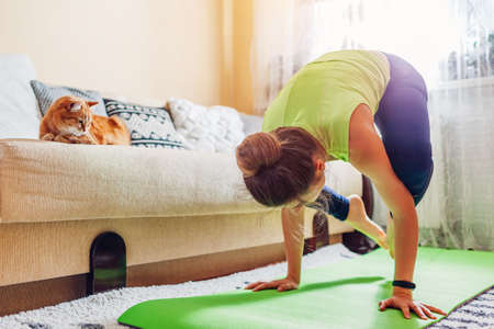 Home yoga workout during virus  lockdown. Kakasana crow pose. Woman training using mat by cat. Balance standing on handsの写真素材